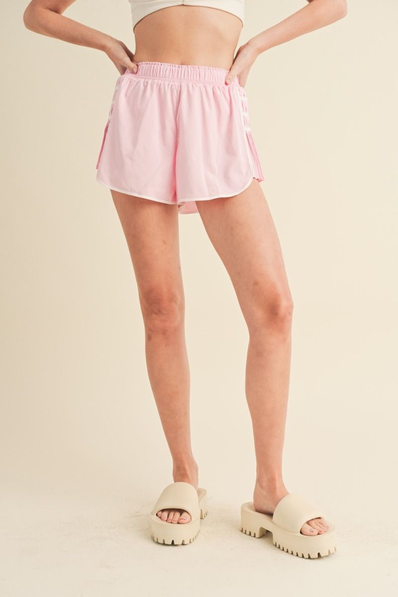 Pink athletic shorts with smocked elastic waistband, contrast seams, and on-trend pleated side details. Front view.