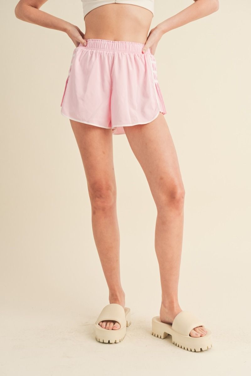 Pink athletic shorts with smocked elastic waistband, contrast seams, and on-trend pleated side details.  Front view.