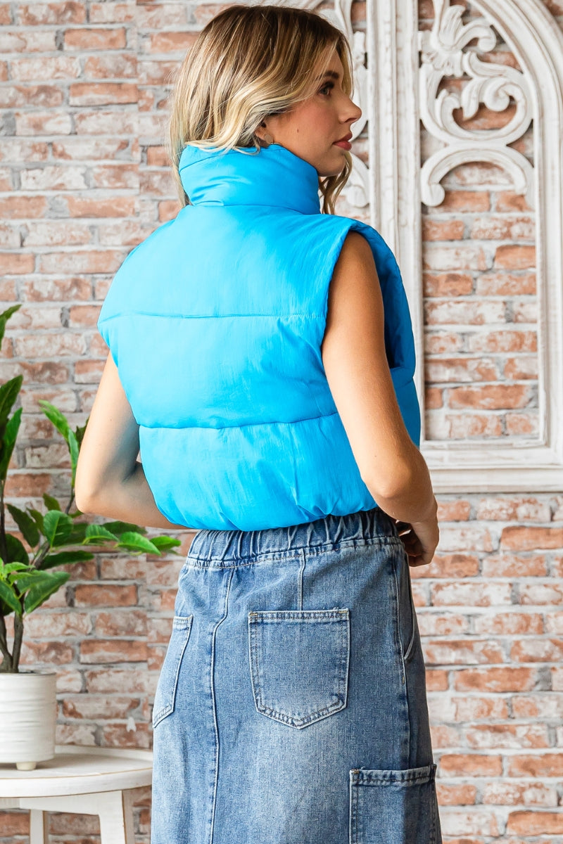 Cropped, mock-neck puffer vest in azure featuring zippered front closure and drawstring cords.  Back view.