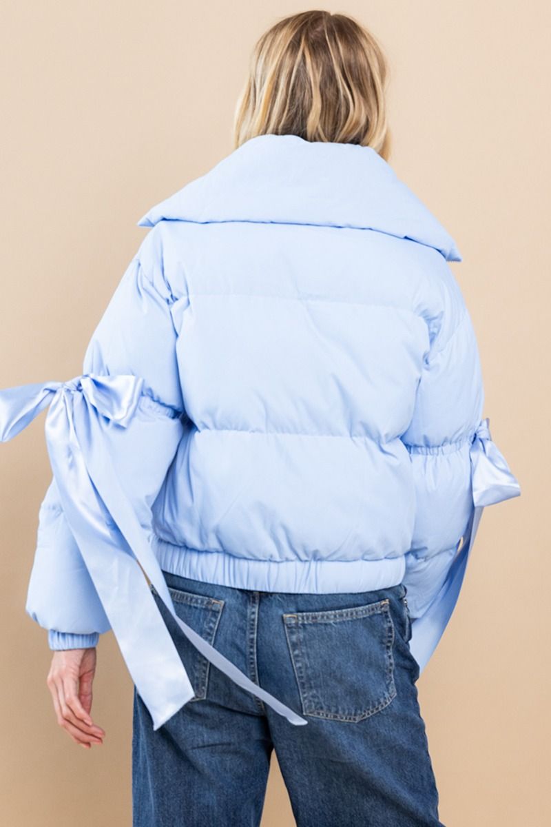 Collared, puffer jacket in baby blue with bow knot elbow string. Zipper and button closure. Featuring side pockets.  Back view.