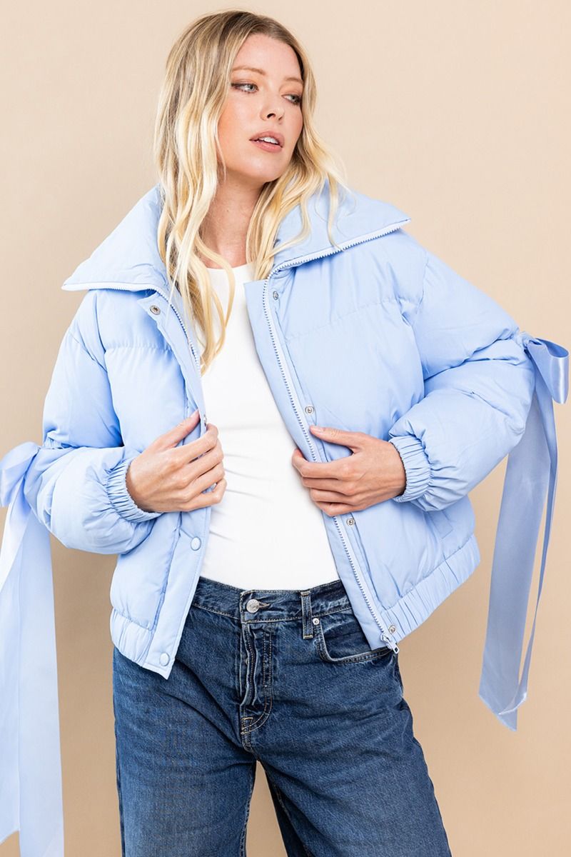 Collared, puffer jacket in baby blue with bow knot elbow string. Zipper and button closure. Featuring side pockets.