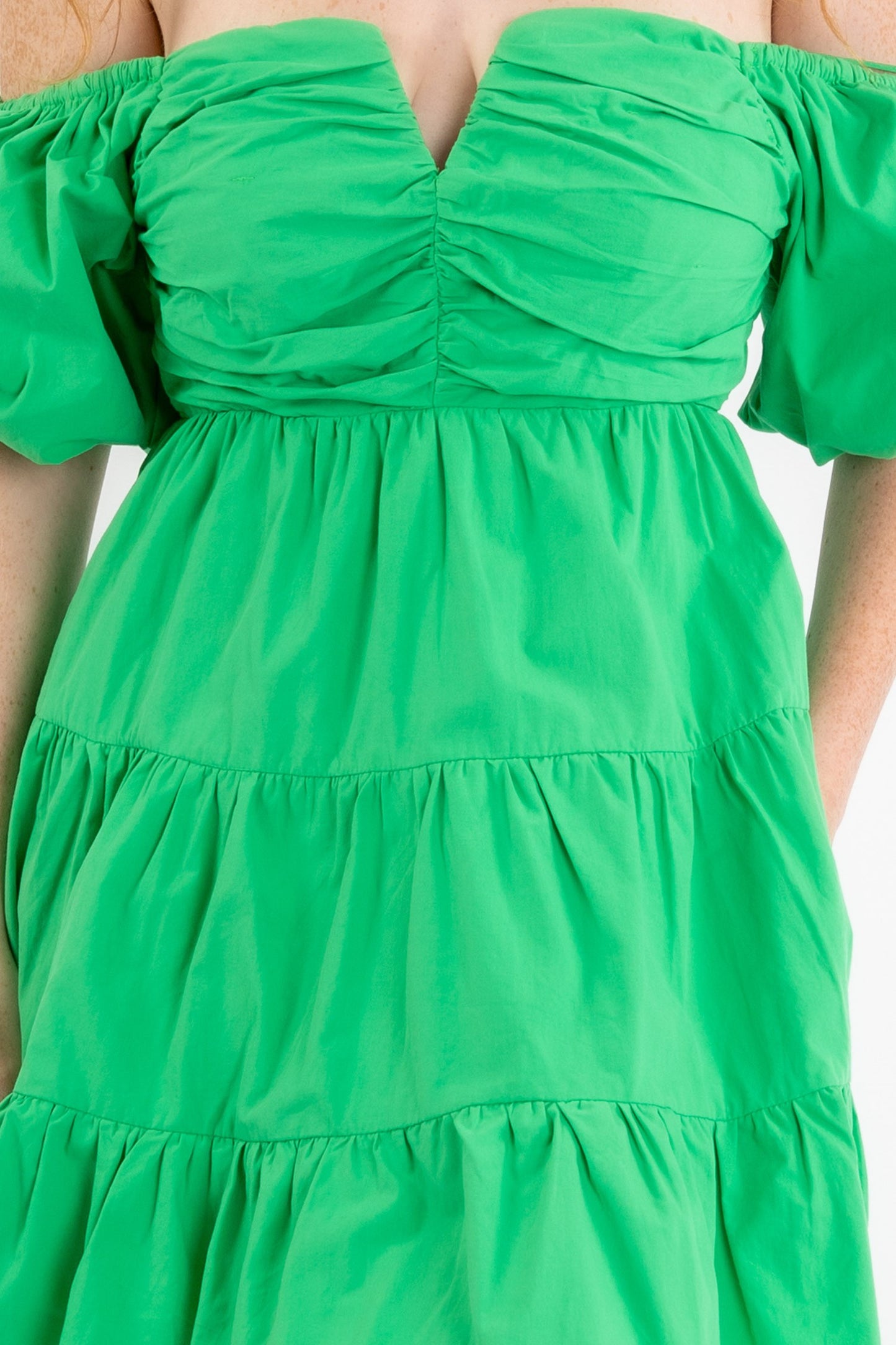 Poplin mini dress in green featuring a v-trim front and puff sleeves that can be worn on or off the shoulder. Close up view.