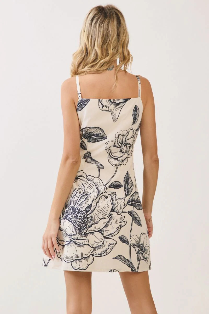 Woman standing in a cream patterned dress, back view