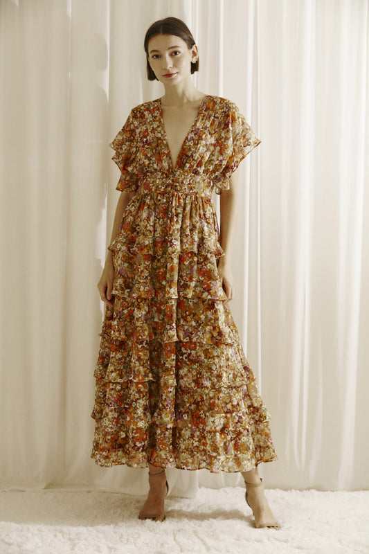 Ditsy floral print midi dress multicolor. Prominent browns, oranges, purples, and maroons.  It shows a deep v-neckline, short fluttered, ruffled sleeves, and a cinched empire waist with center buttons. It also has a ruffled, tiered layered, midi bottom and an open back with a crisscross back tie..  Front full view.