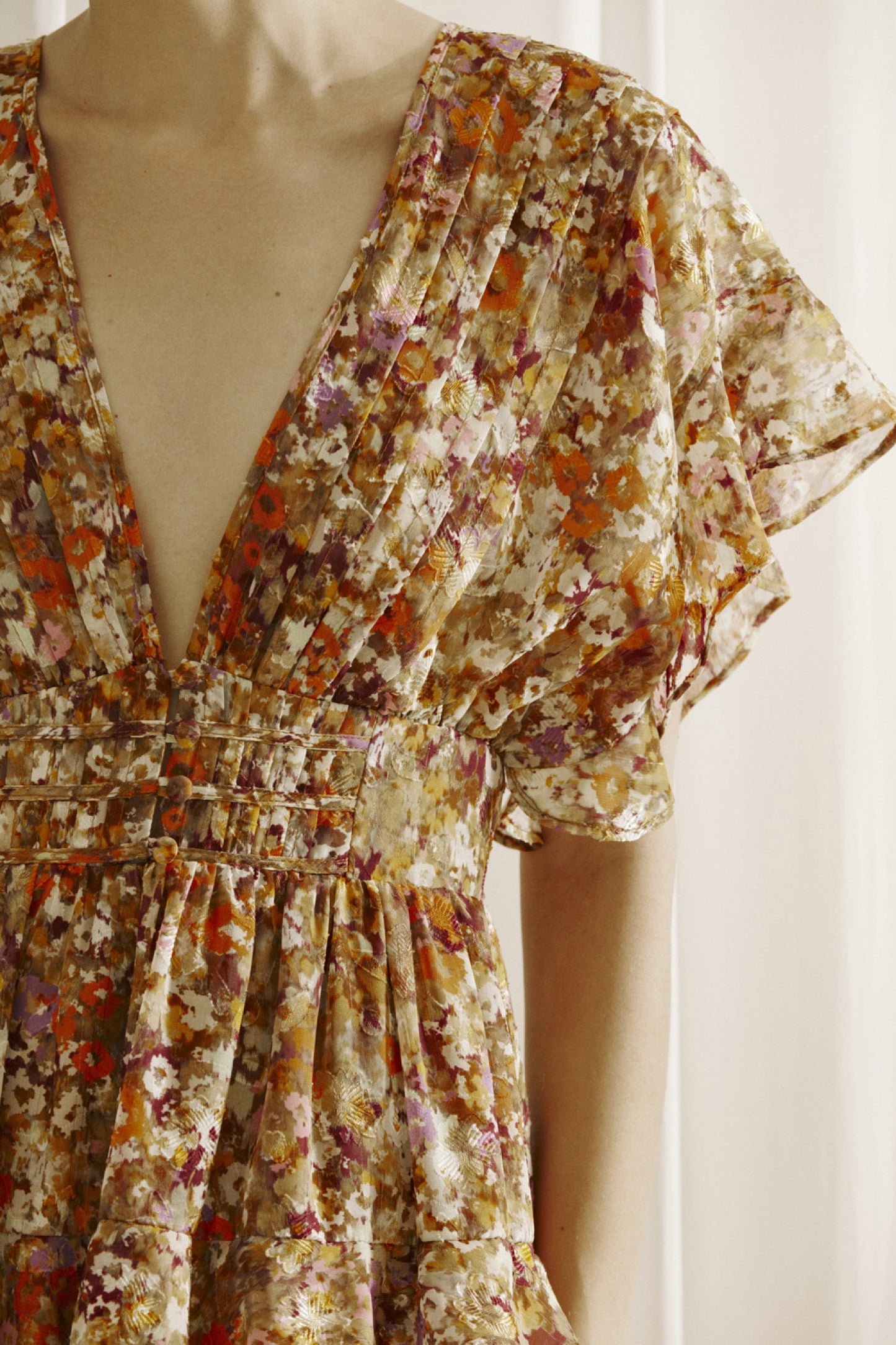 Ditsy floral print midi dress multicolor. Prominent browns, oranges, purples, and maroons.  It shows a deep v-neckline, short fluttered, ruffled sleeves, and a cinched empire waist with center buttons. It also has a ruffled, tiered layered, midi bottom and an open back with a crisscross back tie..  Front close view.
