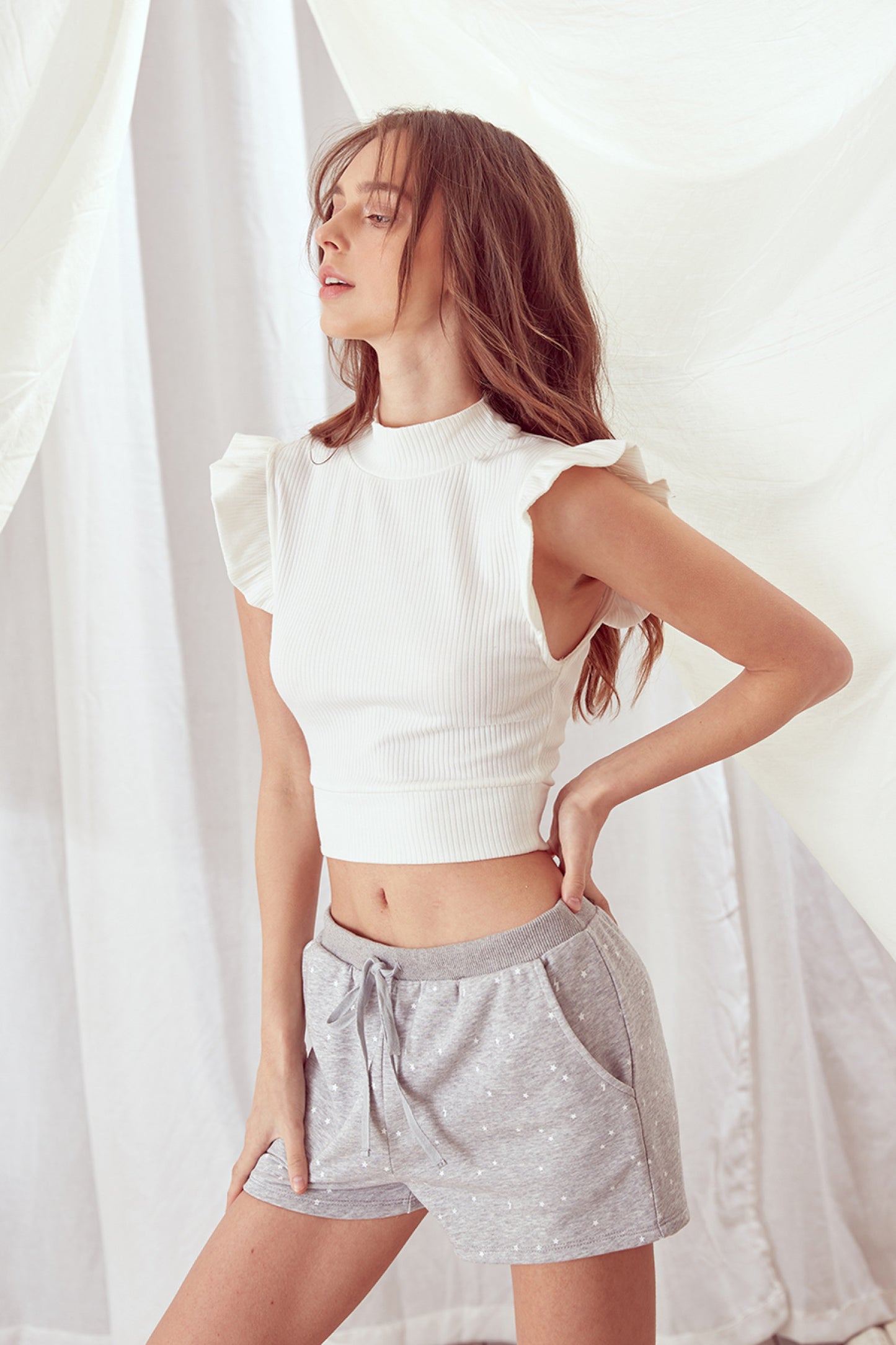 Ribbed knit mock neck crop top in white featuring ruffle sleeves. Front close view.