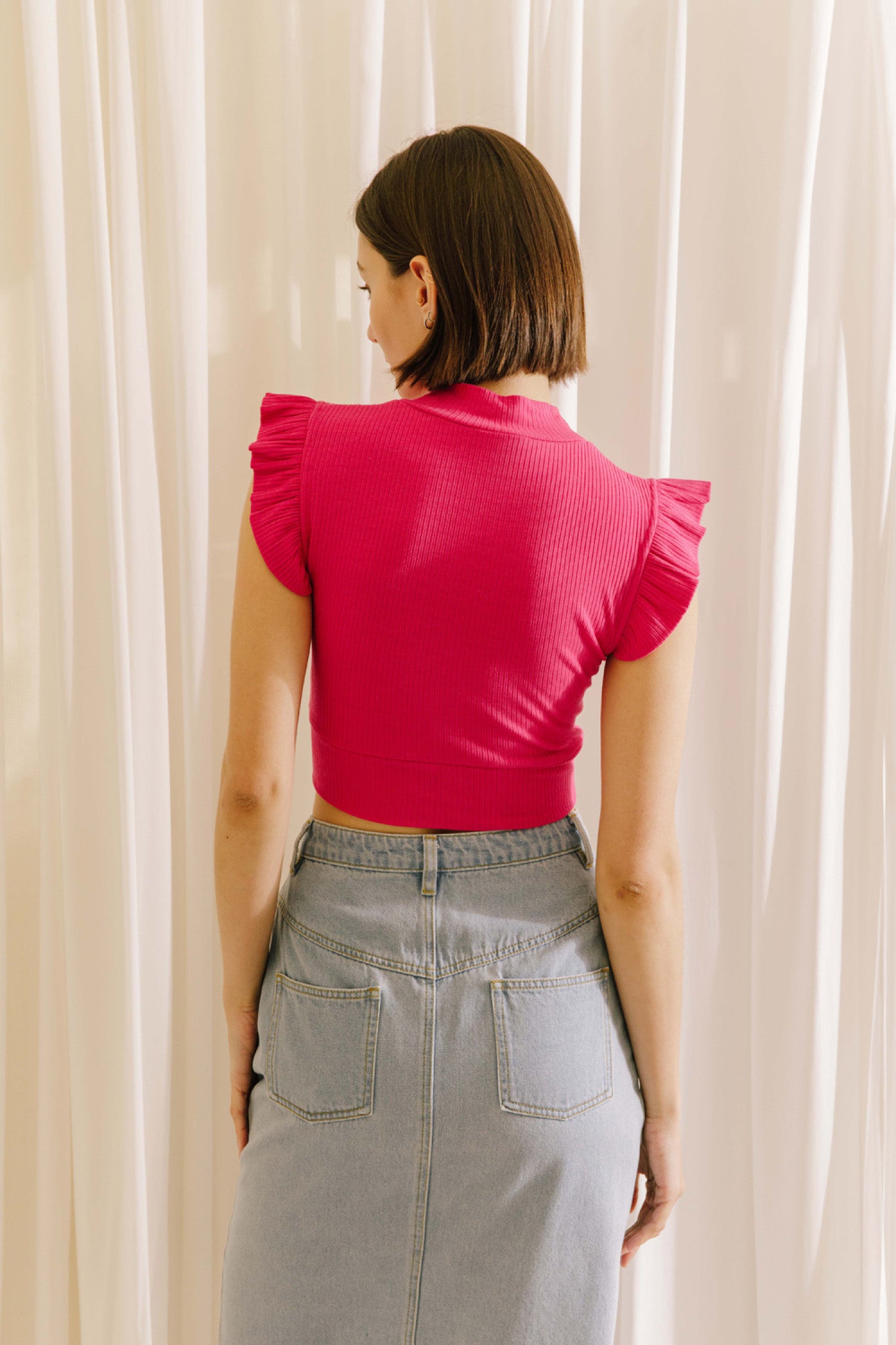 Ribbed knit mock neck crop top in fuchsia featuring ruffle sleeves.  Back view.