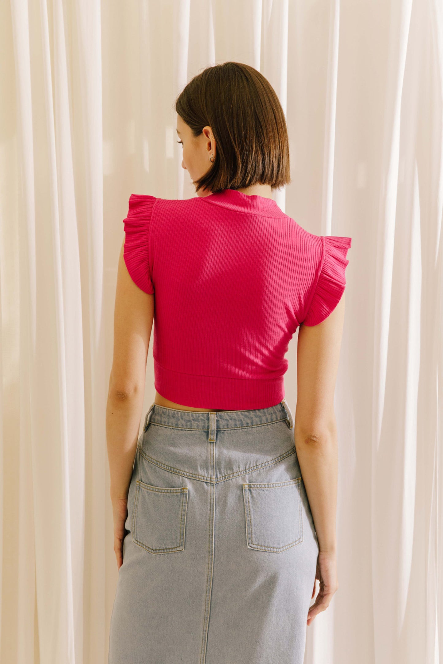 Ribbed knit mock neck crop top in fuchsia featuring ruffle sleeves.  Back view.