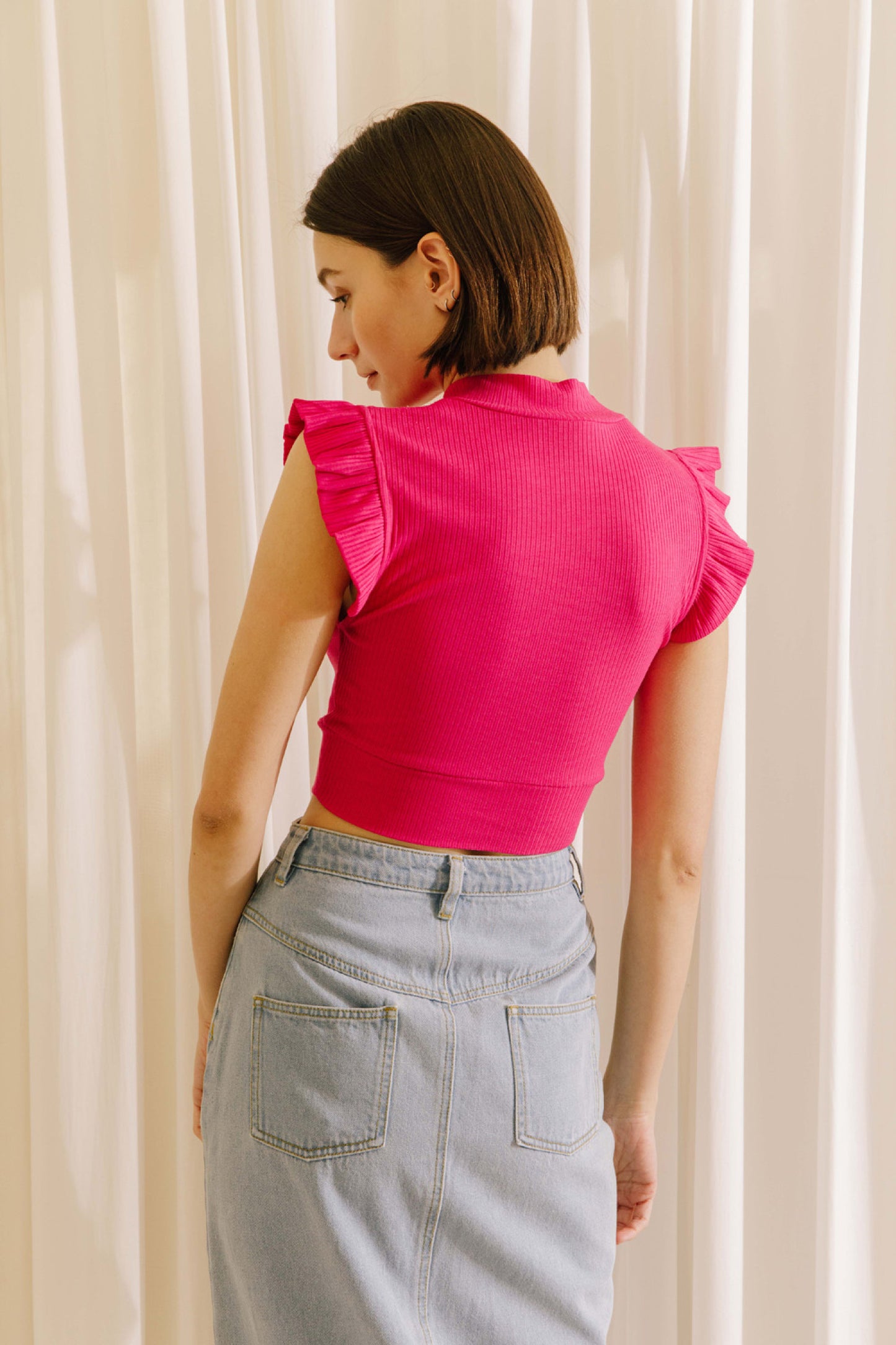 Ribbed knit mock neck crop top in fuchsia featuring ruffle sleeves.  Back close view.