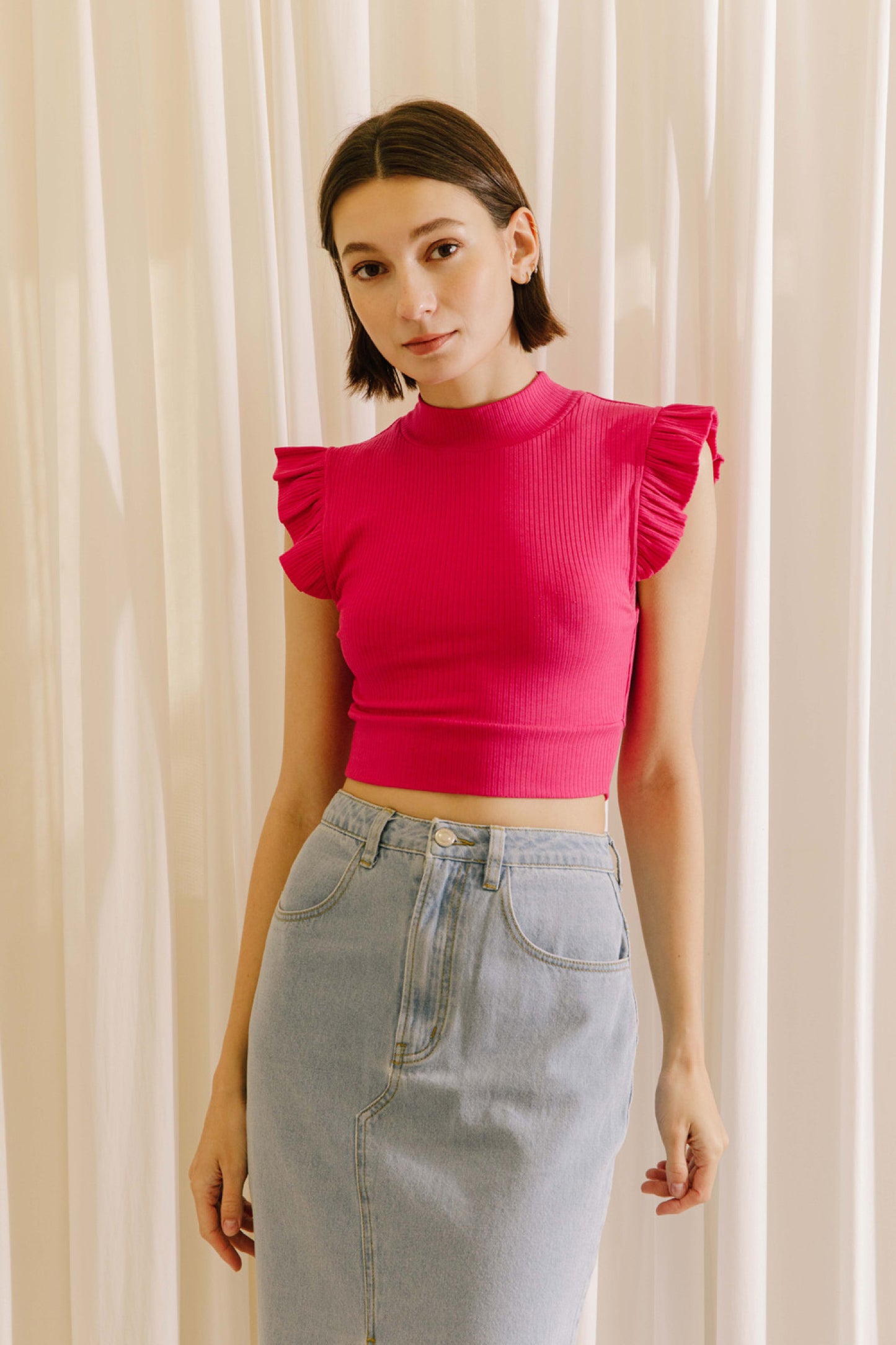 Ribbed knit mock neck crop top in fuchsia featuring ruffle sleeves.  Front view.