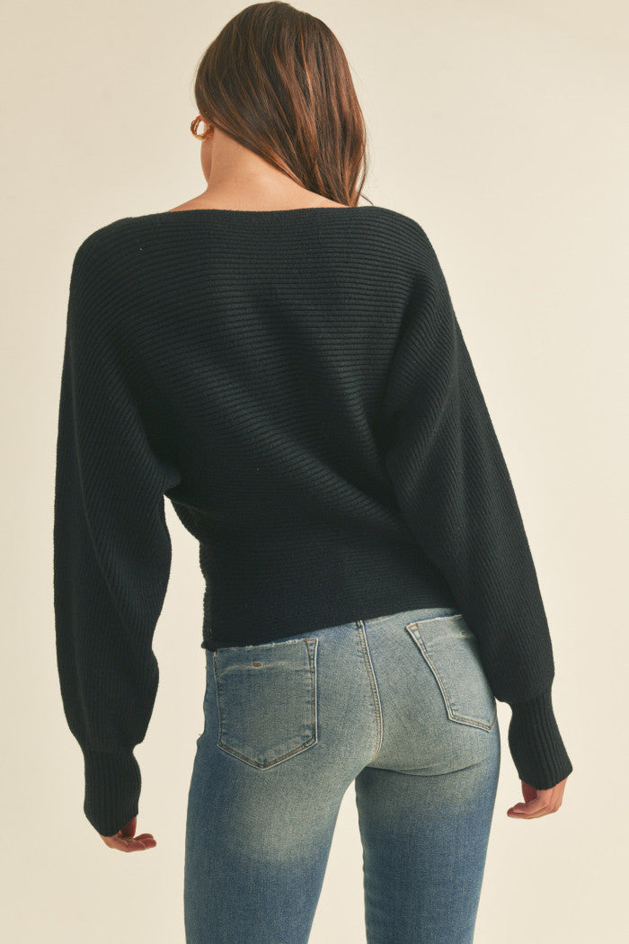 Ribbed sweater in black with long dolman-style sleeves, boat neckline, relaxed bodice, and a fitted waist.  Back view.