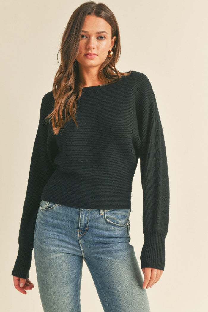 Ribbed sweater in black with long dolman-style sleeves, boat neckline, relaxed bodice, and a fitted waist.  Front view.