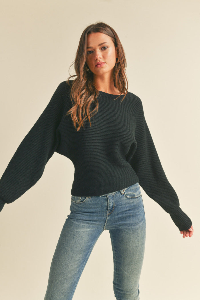 Ribbed sweater in black with long dolman-style sleeves, boat neckline, relaxed bodice, and a fitted waist.  Front view.