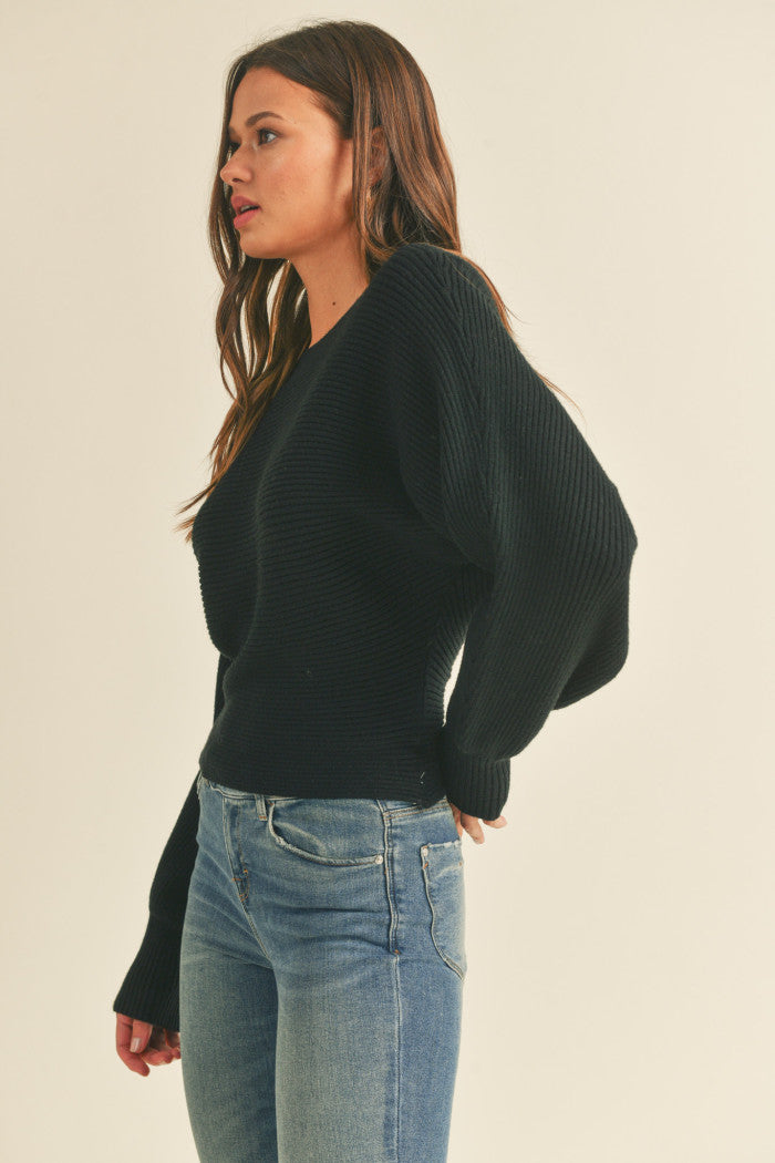 Ribbed sweater in black with long dolman-style sleeves, boat neckline, relaxed bodice, and a fitted waist.  Side view.