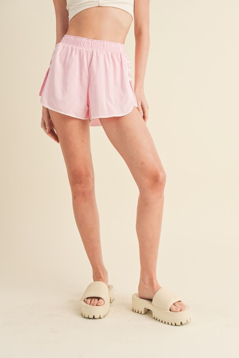 Pink athletic shorts with smocked elastic waistband, contrast seams, and on-trend pleated side details.  Front full view.